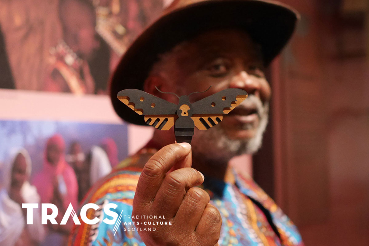 African storyteller Chief Gift Amu holding a delicate papercut moth artwork created by wildlife artist Ed Harrison.